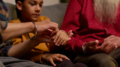 Close-Up-Of-Multi-Generation-Male-Sikh-Family-Wearing-And-Discussing-Traditional-Silver-Bangles-Or-Bracelets-Sitting-On-Sofa-At-Home-3